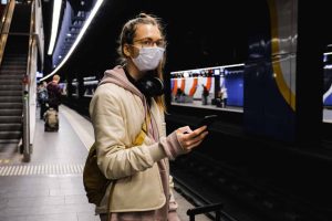 Young woman wearing anti-bacterial face mask is checking her phone while waiting for her ride